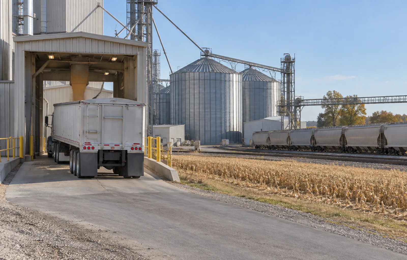 Illustrative view of an unbranded grain hopper truck at an inland elevator, with grain railcars and silos on a separate track.