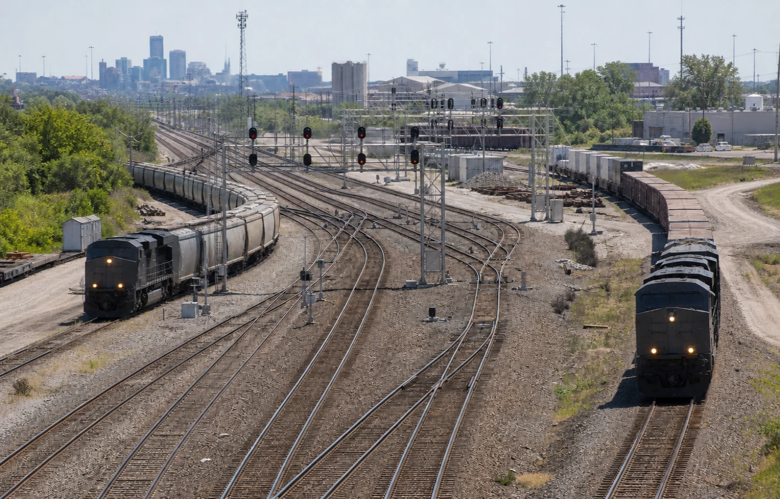 Two unbranded freight trains approach a large rail junction from separate routes beneath signal gantries.